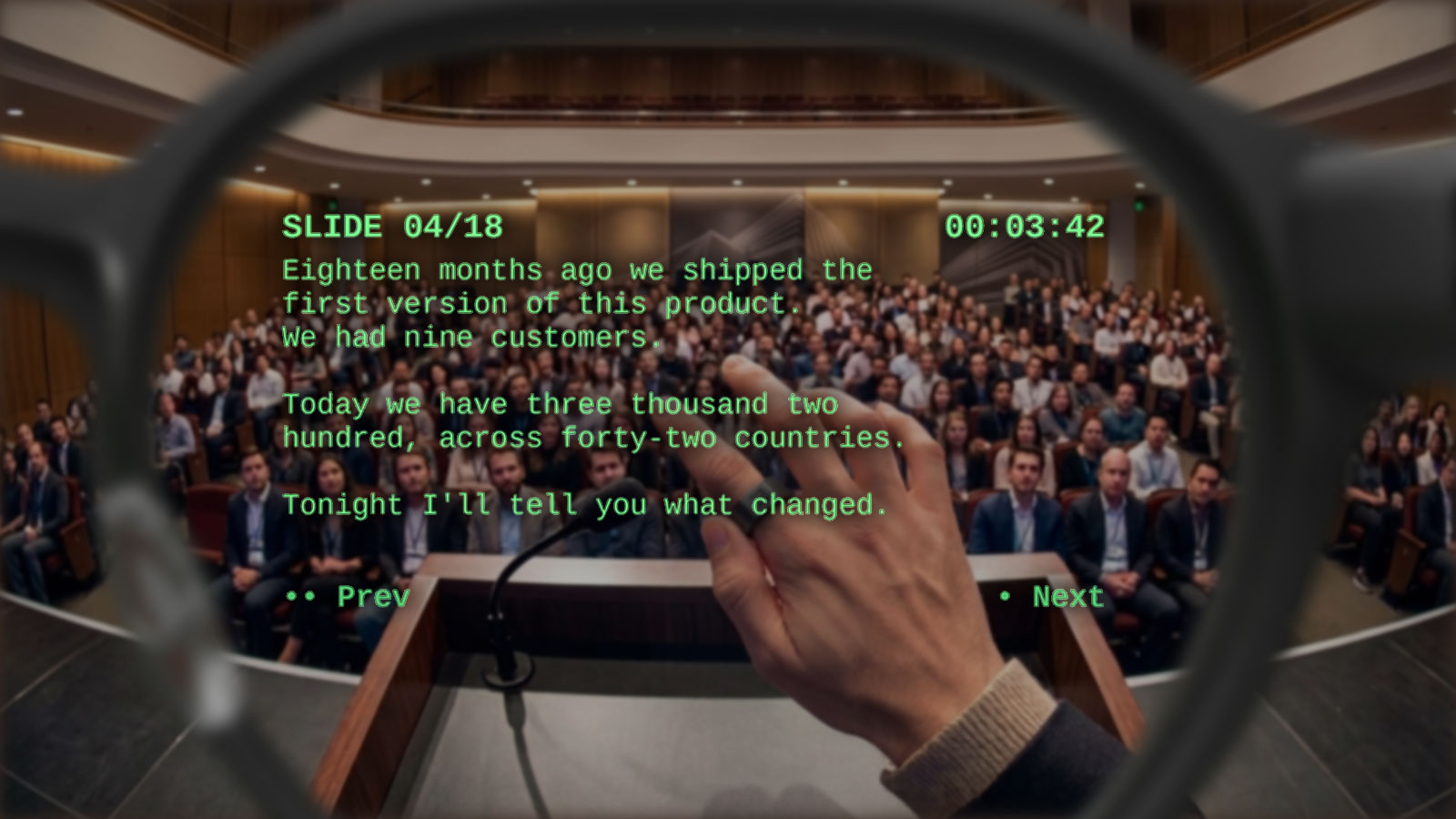 Point-of-view through Even Realities G2 glasses: audience in soft bokeh in the background, a HUD overlay in the foreground showing scrolling speaker notes on the left and a footer with SLIDE 12/42 and the timer 00:12:34